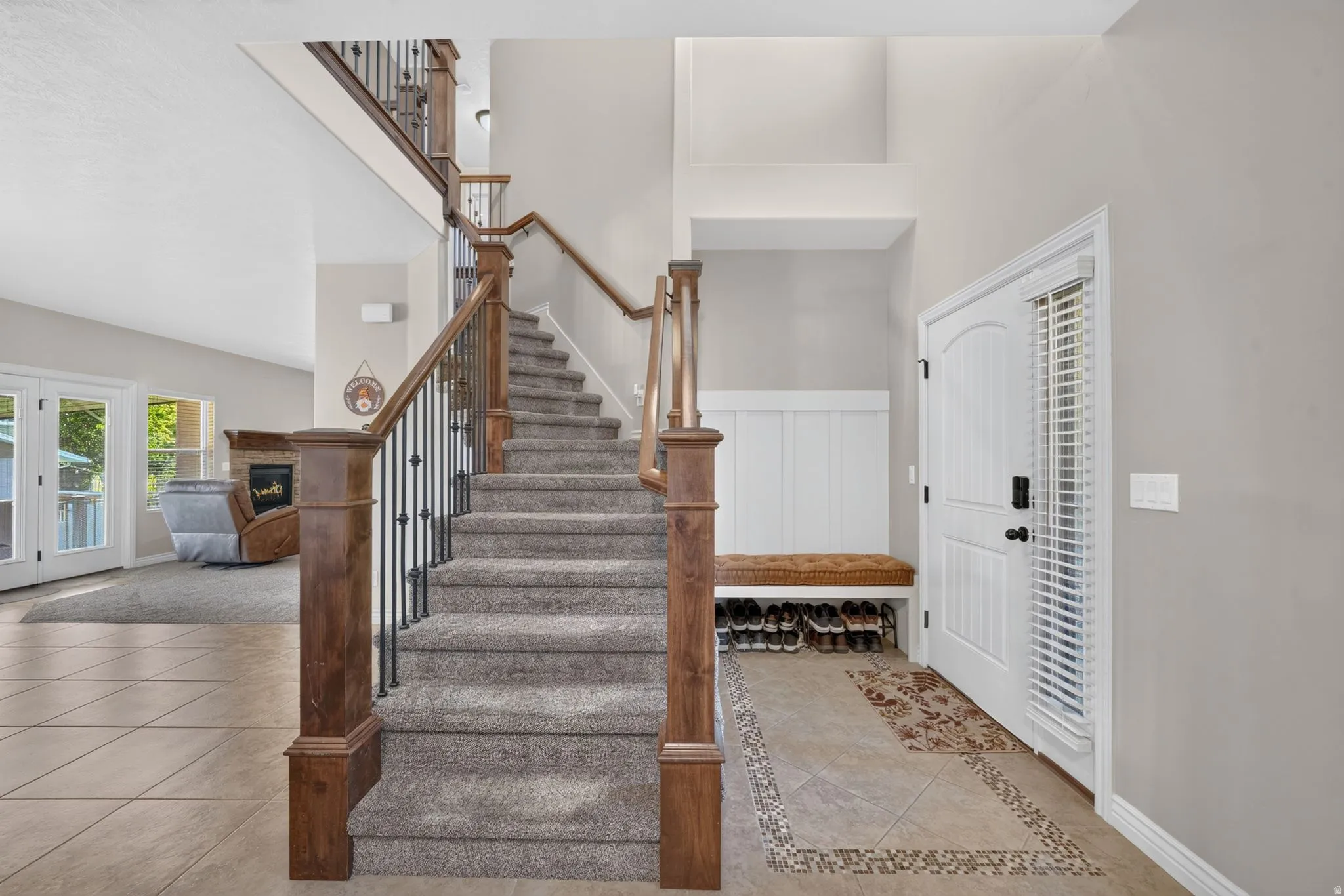 Two-story foyer featuring a carpeted staircase with wood and iron railings, tile flooring with an inlaid accent, and a built-in bench with shiplap backing