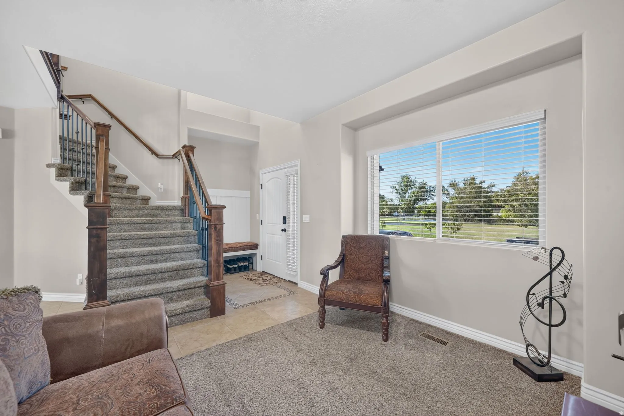 Staircase with wood newel posts and iron balusters, foyer with tiled flooring, built-in bench, and a window offering outdoor scenery