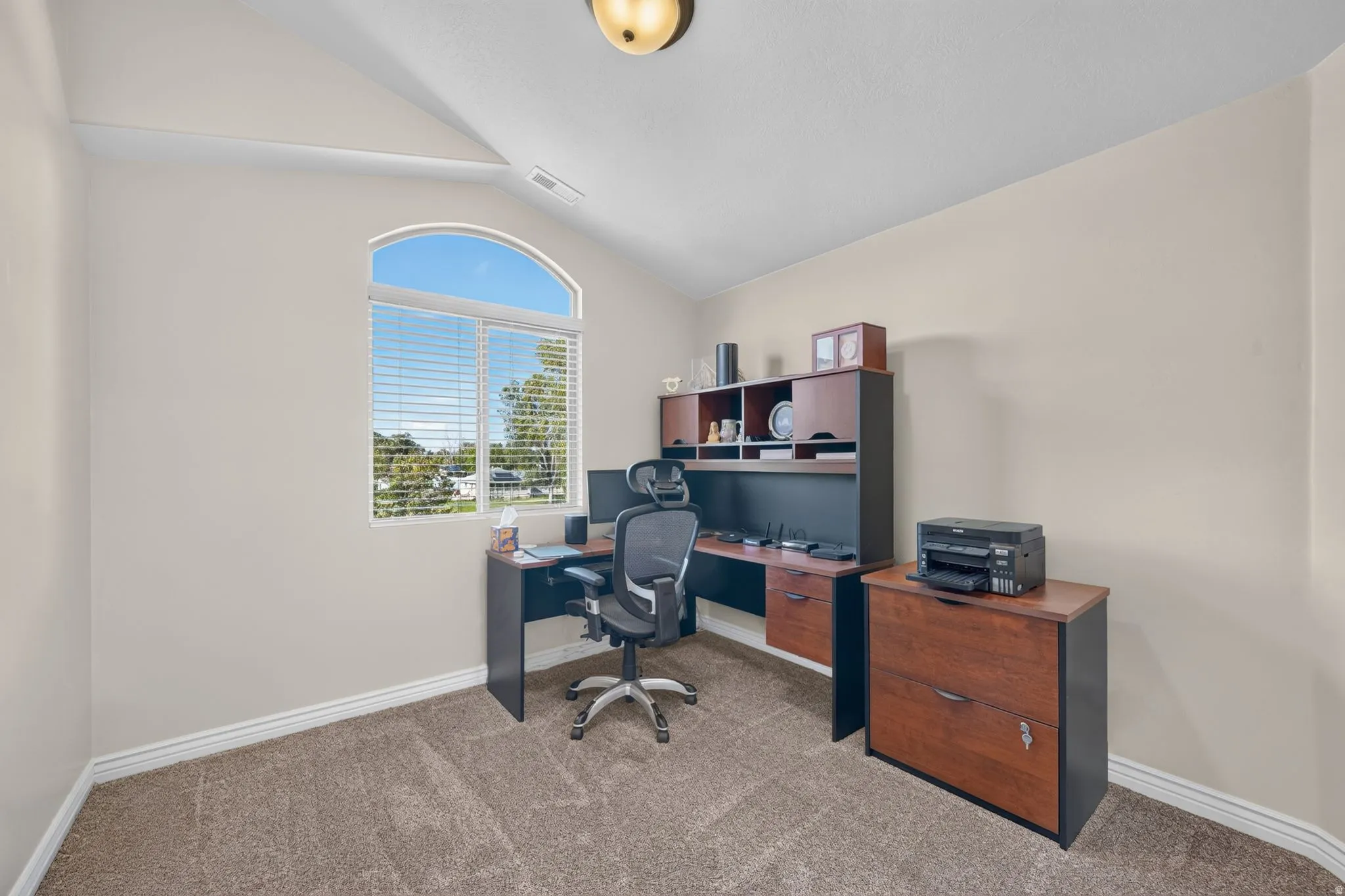 Arched window with blinds, vaulted ceiling, and neutral carpet flooring