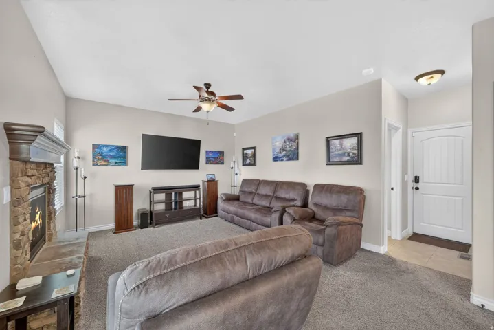 Vaulted ceiling with a ceiling fan, stone-faced fireplace with a wood mantle, neutral wall paint, and carpet flooring