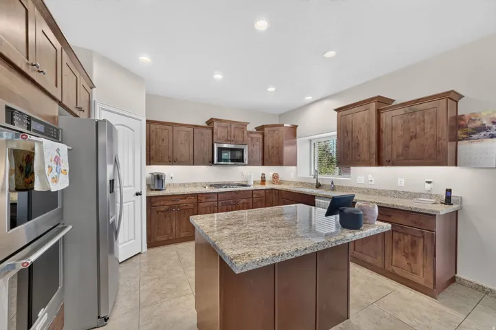 Kitchen featuring recessed lighting, extensive wood cabinetry, an island with a stone countertop, and stainless steel appliances
