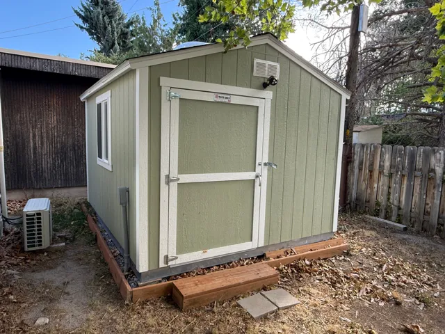 Exterior storage shed featuring a single window, hinged door, and exterior lighting fixture