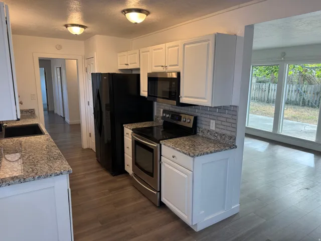 Kitchen featuring white cabinetry, granite-finish countertops, stainless steel appliances, and a tiled backsplash