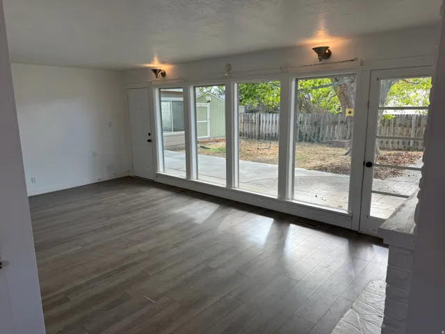 Wood-finish flooring throughout, white painted walls, multiple large windows, glass-paneled door, and a white painted brick fireplace