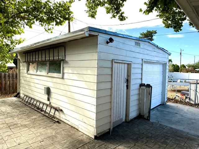 Detached outbuilding with white siding, single garage door, side entry door, and multiple windows