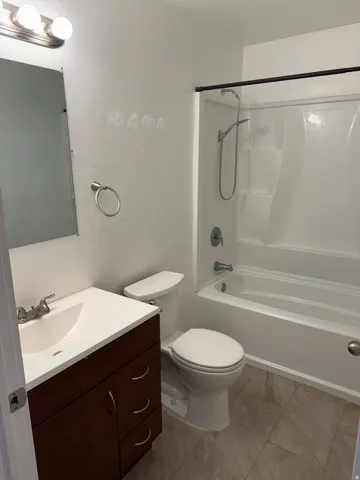 Bathroom featuring a dark wood-finish vanity with an integrated sink, a white toilet, and a white bathtub with a shower