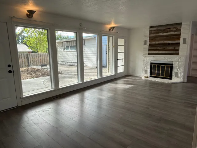 Wood-finish flooring, white brick fireplace with a wood panel accent, built-in shelving, and multiple large windows with a glass-paneled door