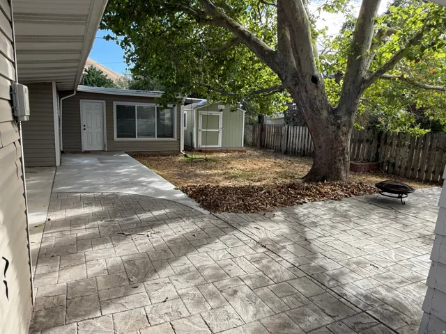 Stamped concrete patio with an established shade tree, wood privacy fencing, and a detached storage shed