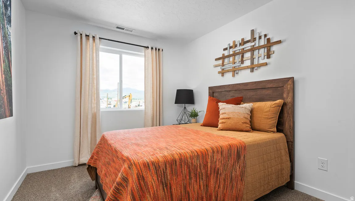 Carpeted flooring, white painted walls, single window with roller shade, and a wood-finish headboard
