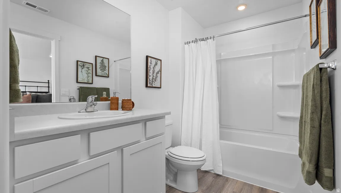White vanity with integrated sink, wood-finish flooring, white bathtub with shower, and recessed lighting