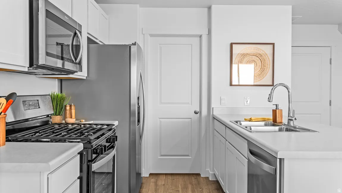 Kitchen featuring white cabinetry, light-toned countertops, stainless steel appliances, and wood-finish flooring