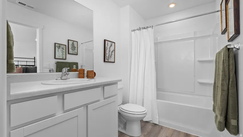 White vanity with integrated sink, wood-finish flooring, white bathtub with shower, and recessed lighting
