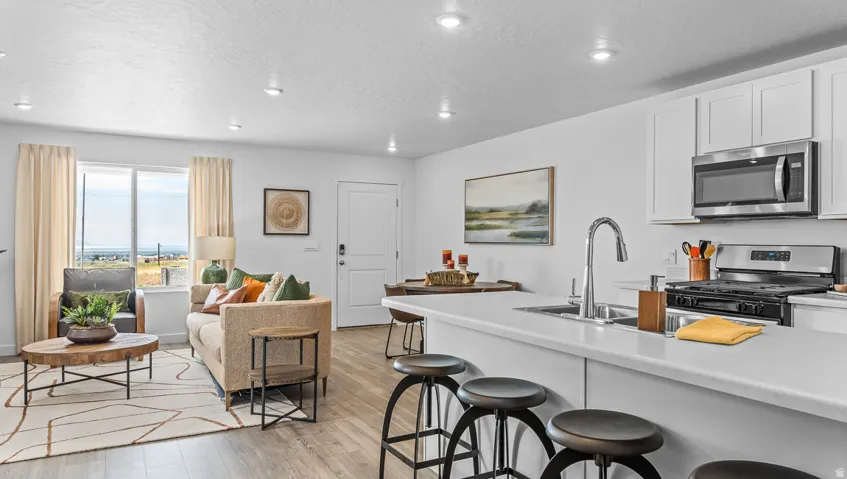 Recessed lighting, wood-finish flooring, stainless steel appliances, kitchen island with sink, and white cabinetry