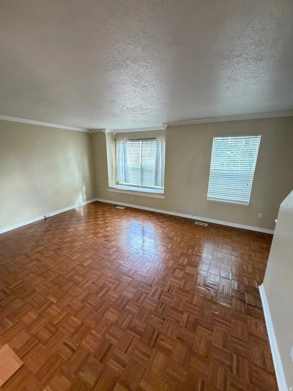 Parquet wood flooring, multiple windows with blinds, crown molding, and neutral wall tones