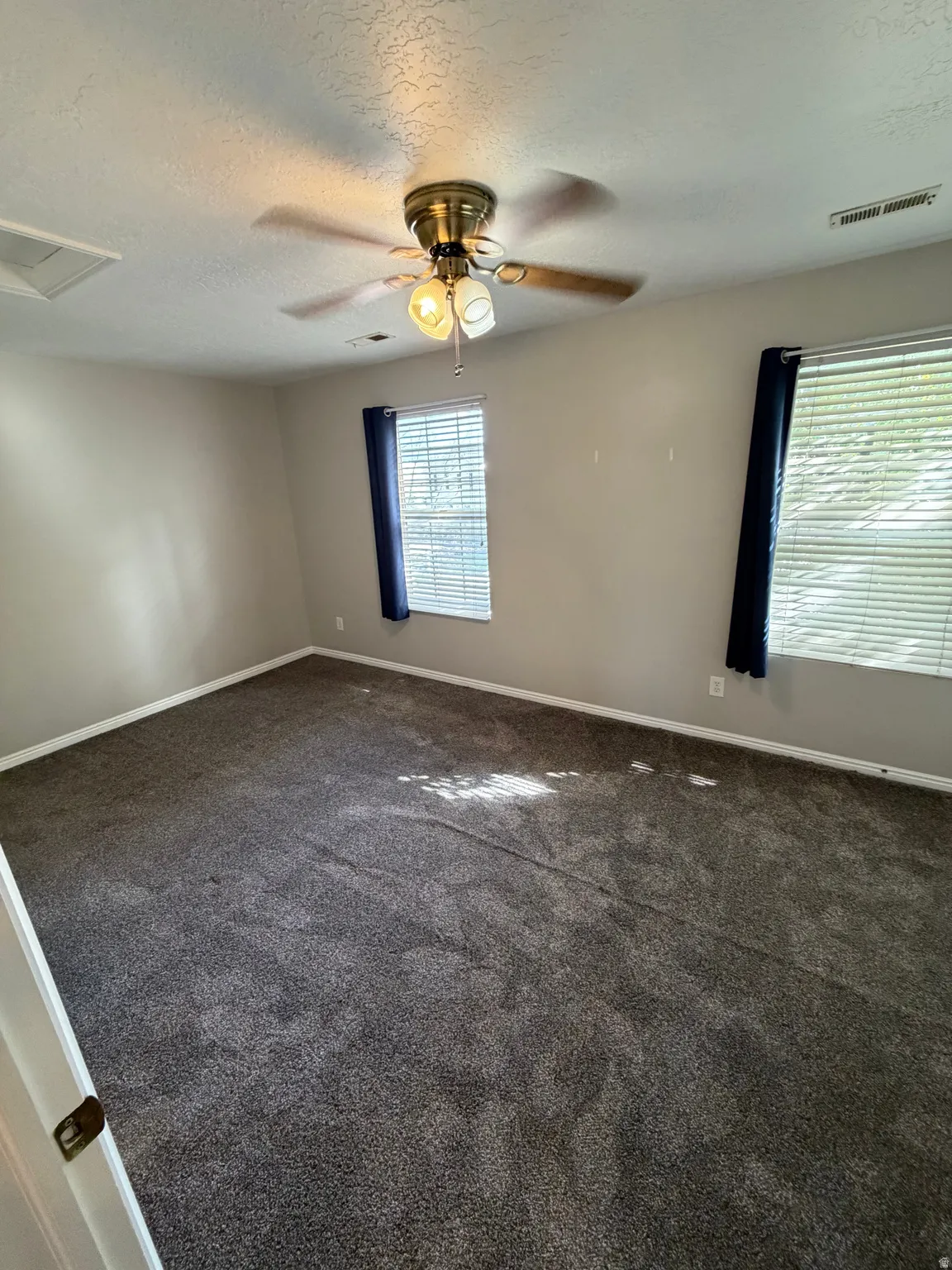 Neutral wall tones, gray carpeting, dual windows with blinds, and a ceiling fan with integrated lighting