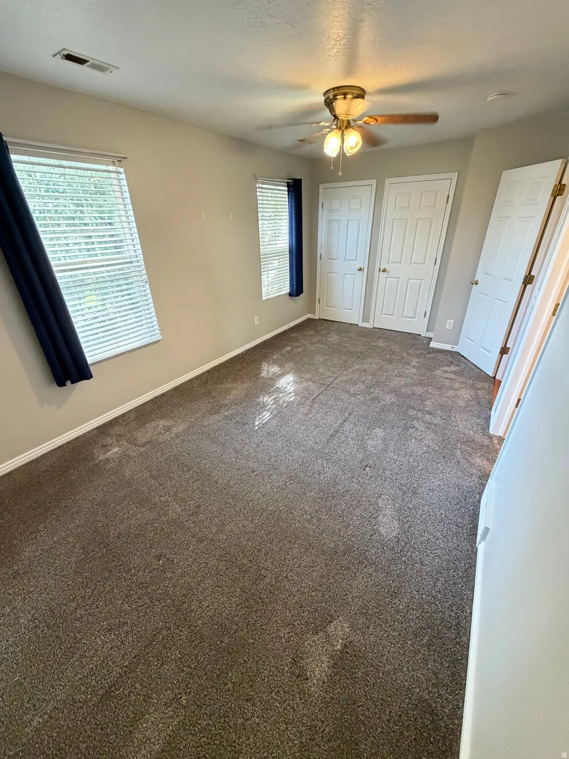 Spacious interior room with neutral-toned walls, brown carpeting, and natural light from multiple windows
