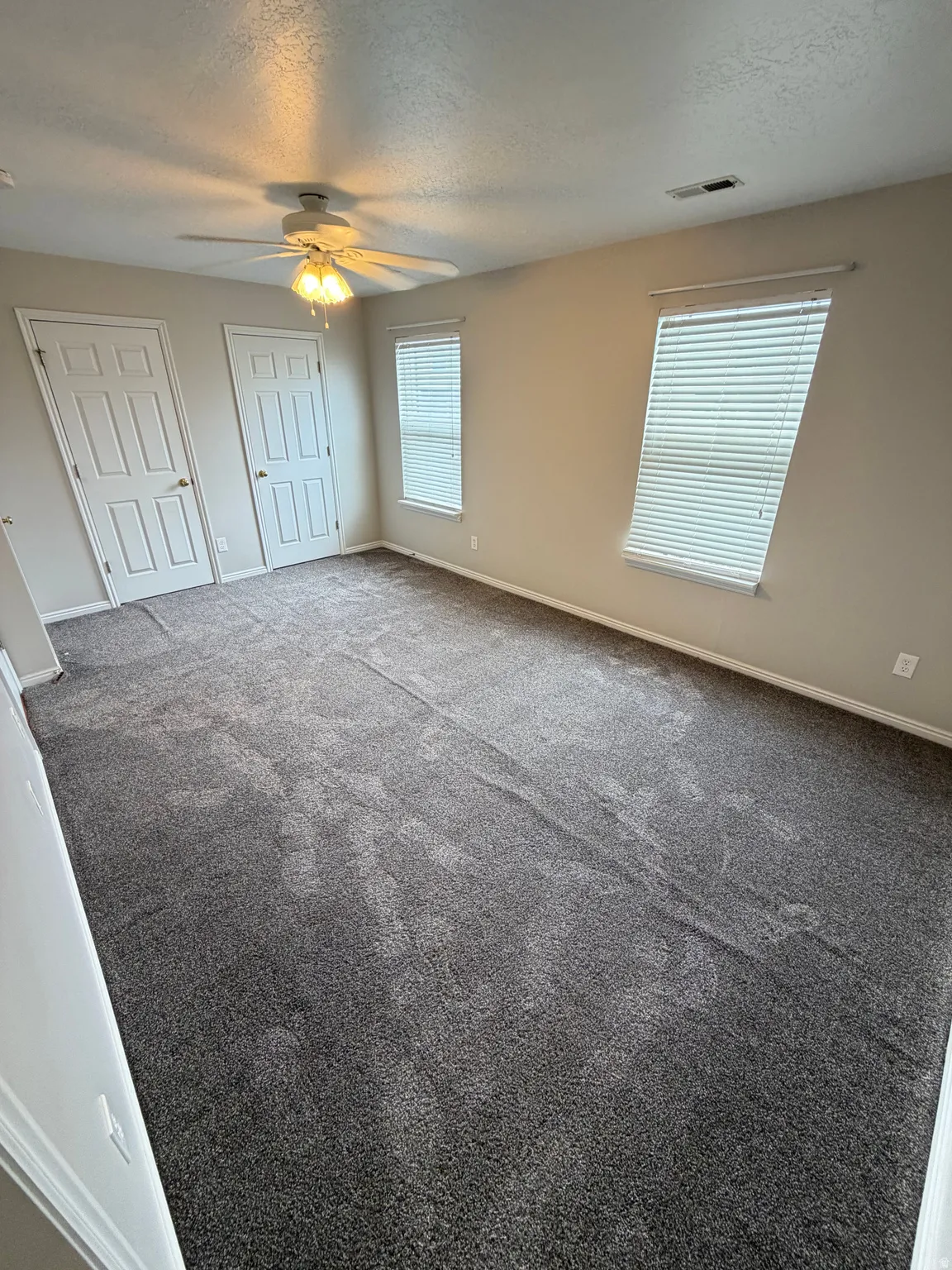 Spacious room featuring neutral carpeting, a ceiling fan with integrated lighting, and multiple windows with blinds