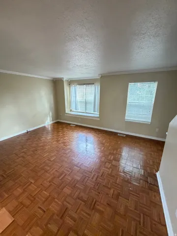 Parquet wood flooring, multiple windows with blinds, crown molding, and neutral wall tones