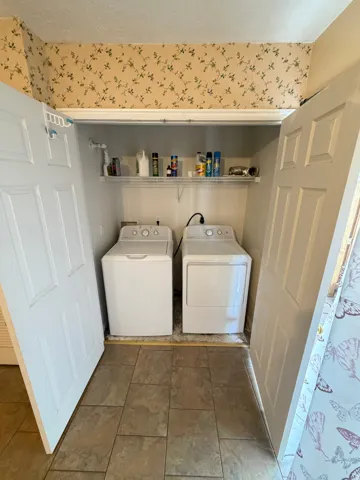 Laundry closet with bi-fold doors, overhead shelving, and tiled flooring