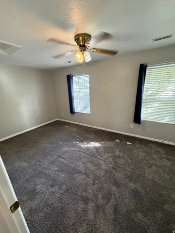 Neutral wall tones, gray carpeting, dual windows with blinds, and a ceiling fan with integrated lighting