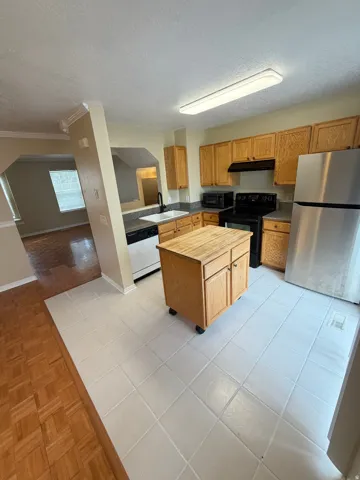 Kitchen featuring tile flooring, light wood-finish cabinetry, stainless steel refrigerator, black range, and black faucet