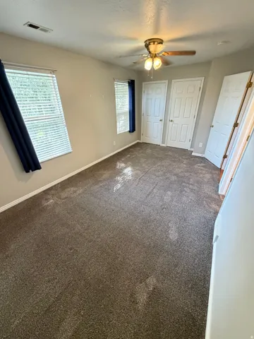 Spacious interior room with neutral-toned walls, brown carpeting, and natural light from multiple windows
