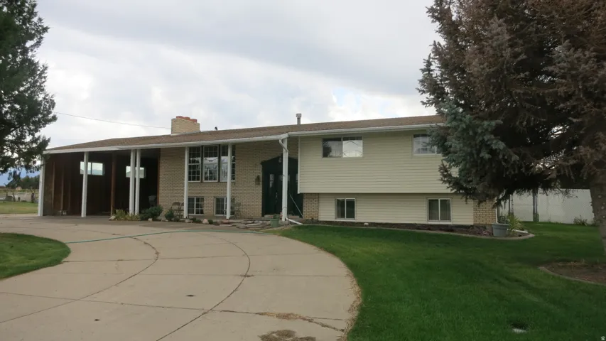 Expansive driveway, brick exterior accents, vinyl siding, mature landscaping, and an attached carport