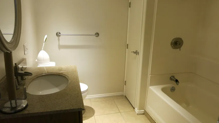 Bathroom featuring a vanity with an undermount sink, a toilet, a bathtub with a shower, and tile flooring
