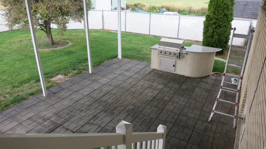 Paved patio with a built-in outdoor kitchen, stainless steel grill, and an expansive lawn
