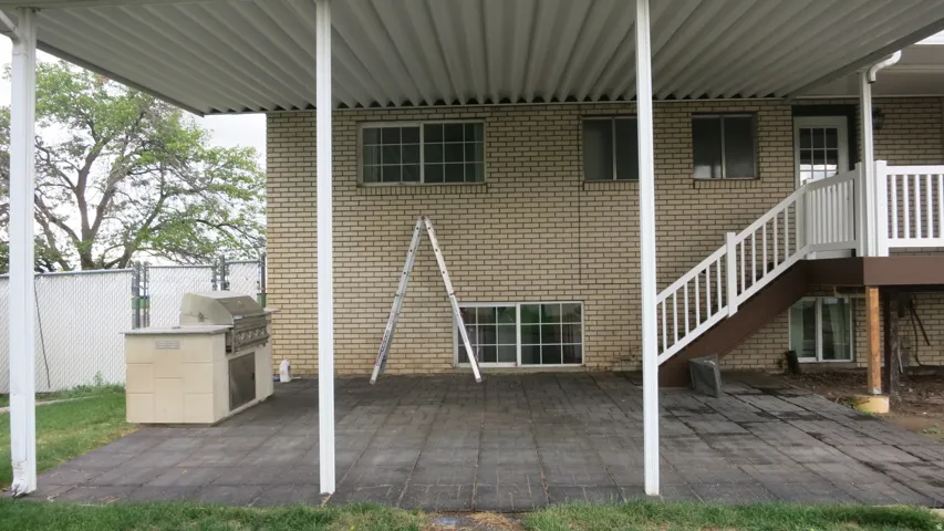 Covered patio with a built-in barbecue station, brick exterior, and white railing staircase