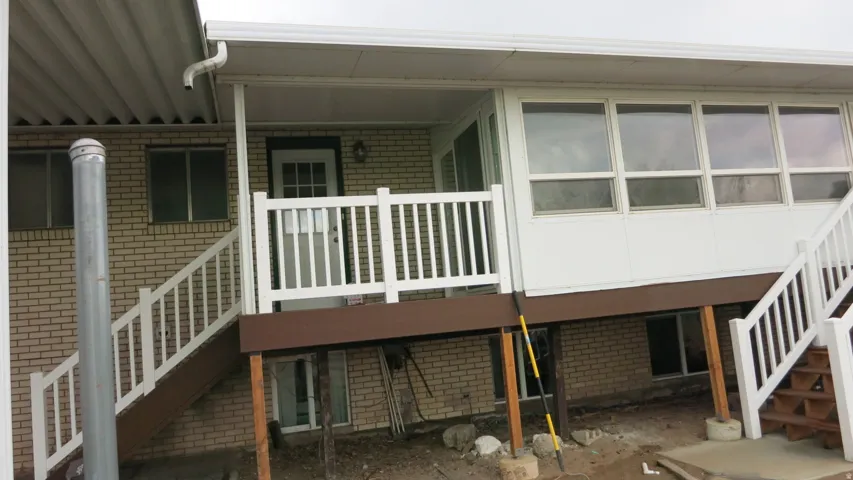 Brick exterior with white trim, white deck railing, and an enclosed sunroom with multiple windows
