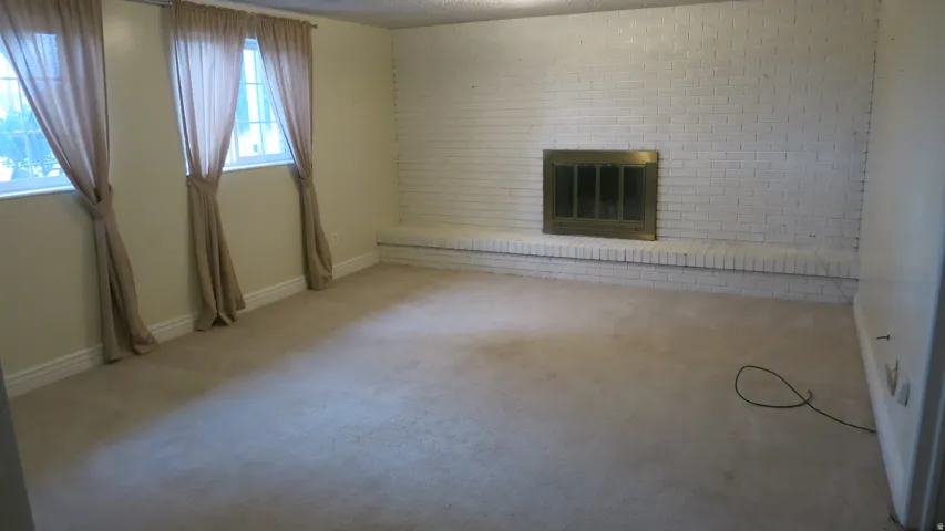 Carpeted room featuring a white painted brick fireplace with a brass firebox and hearth