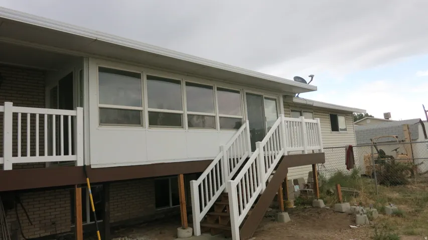 Enclosed patio with multiple windows, leading to a brown wood-finish deck with white railings and stairs