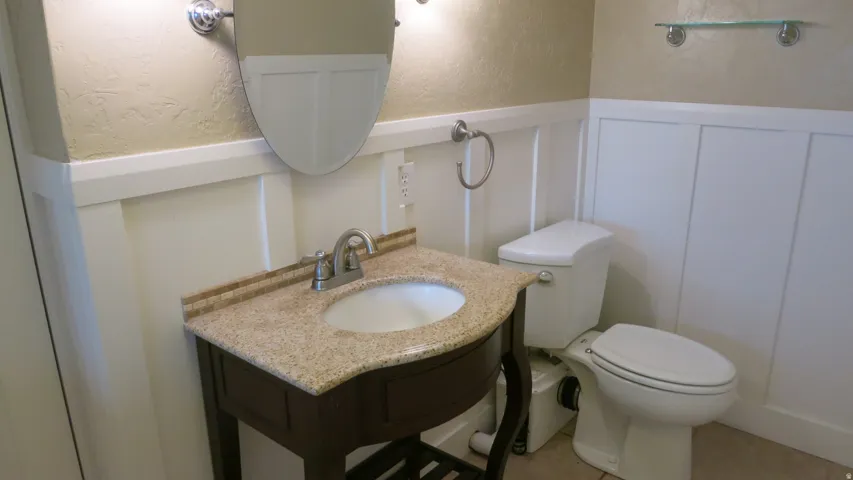 Board and batten wainscoting, vanity with granite countertop, integrated sink, mosaic tile backsplash, and wall-mounted mirror