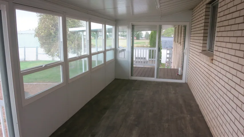 Enclosed patio featuring wood-finish flooring, multiple windows, a sliding glass door, and a brick exterior wall