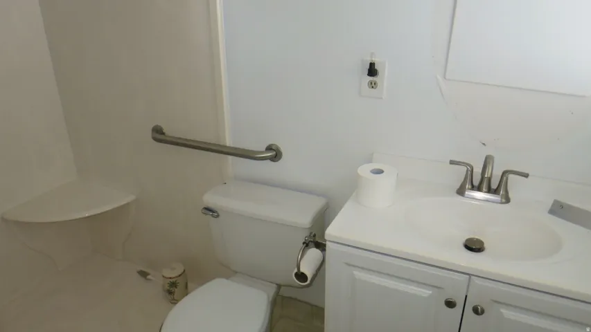 White bathroom featuring a single vanity with storage, chrome fixtures, and a wall-mounted grab bar
