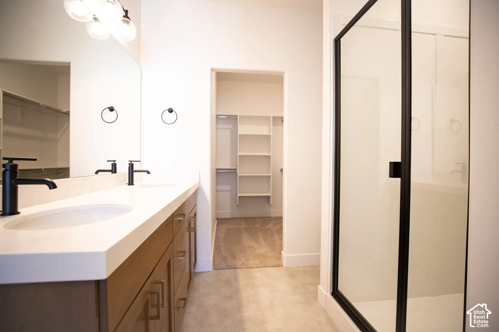 Primary bath with dual sinks, stained wood cabinets, quartz slab countertops, large walk-in shower and spacious walk-in closet as part of primary suite.