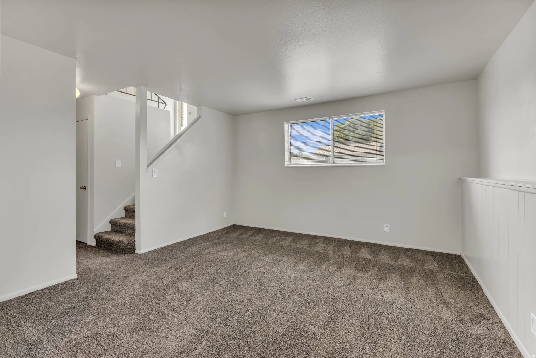 Carpeted flooring, white interior paint, window with blinds, white wainscoting, and carpeted stairs