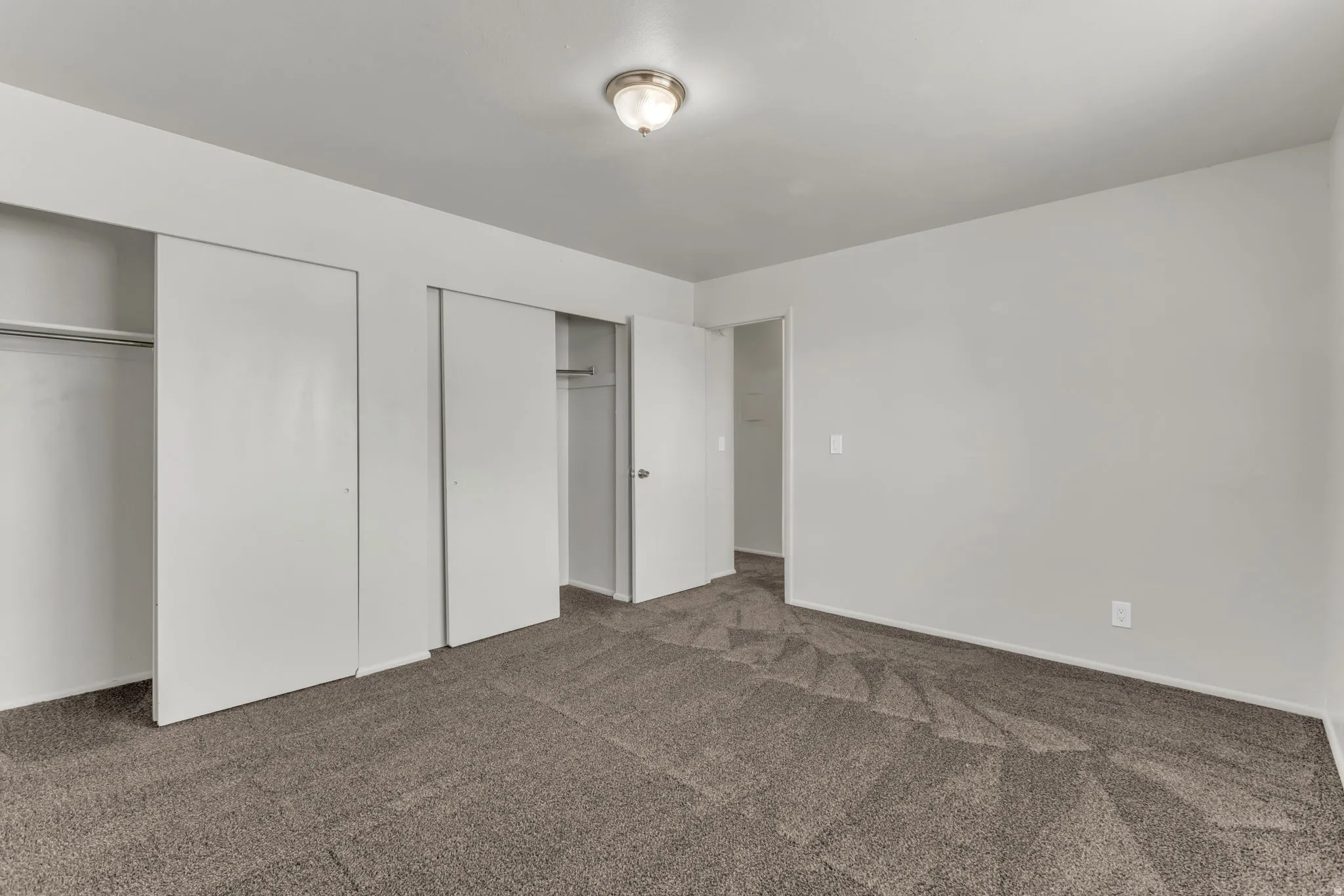 Neutral tone wall paint, textured carpeting, recessed closets with sliding doors, and a ceiling-mounted light fixture