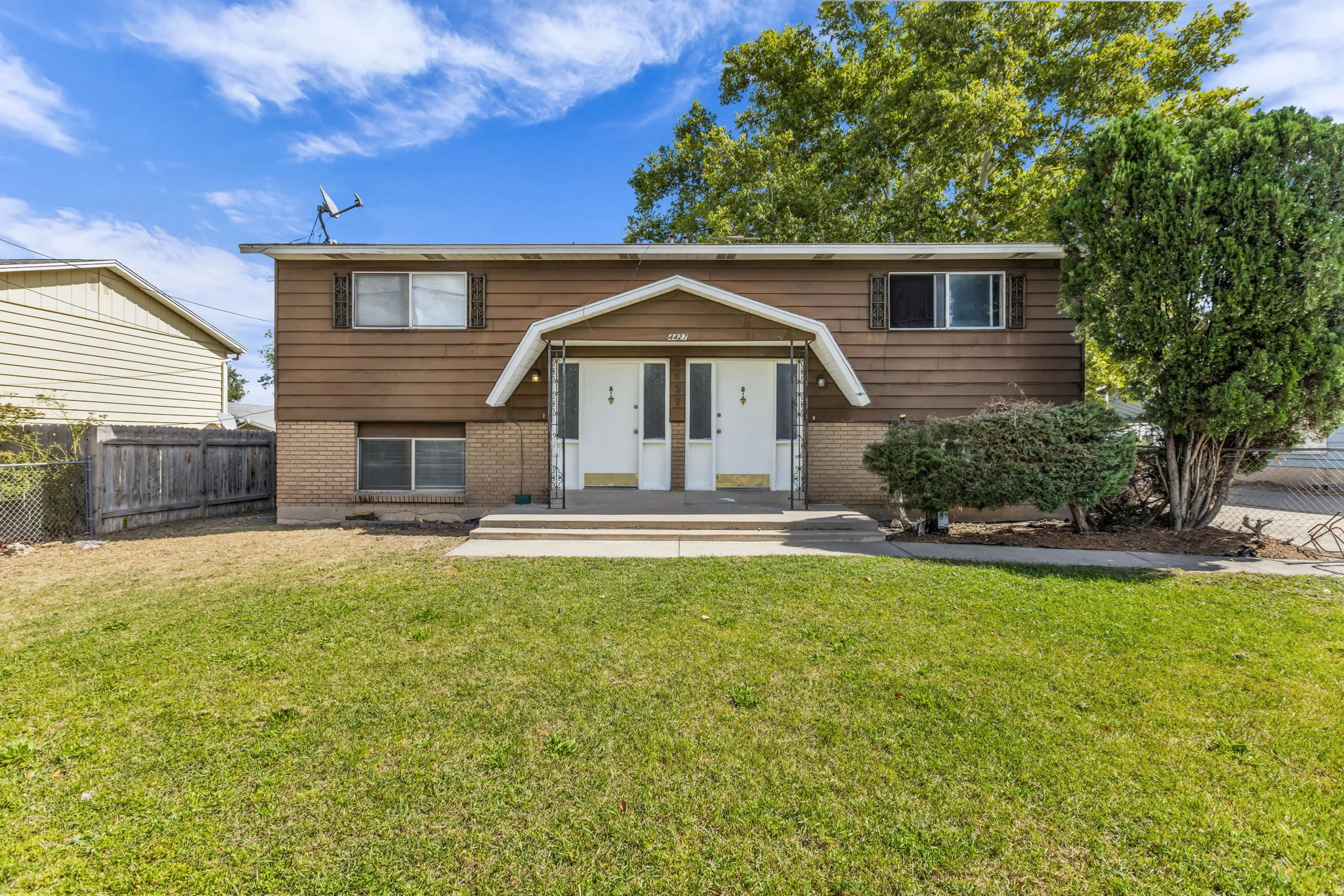 Brown siding exterior with a brick foundation, dual entry doors, and a front lawn