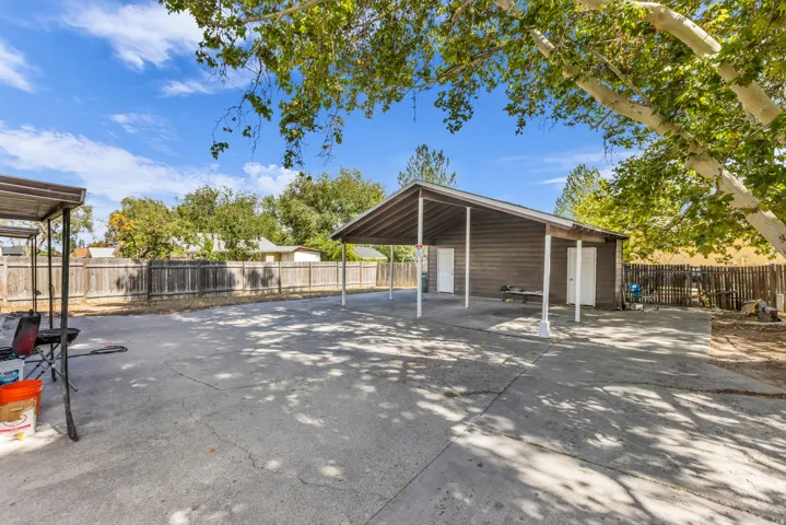 Expansive concrete pad featuring a covered carport structure, an additional covered patio area, and perimeter wood fencing