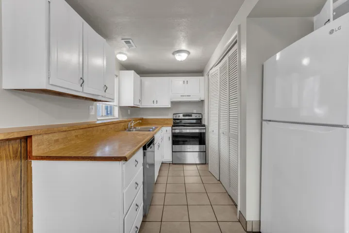 Unit A, Kitchen featuring white cabinetry, wood-finish countertops, stainless steel appliances, and tile flooring