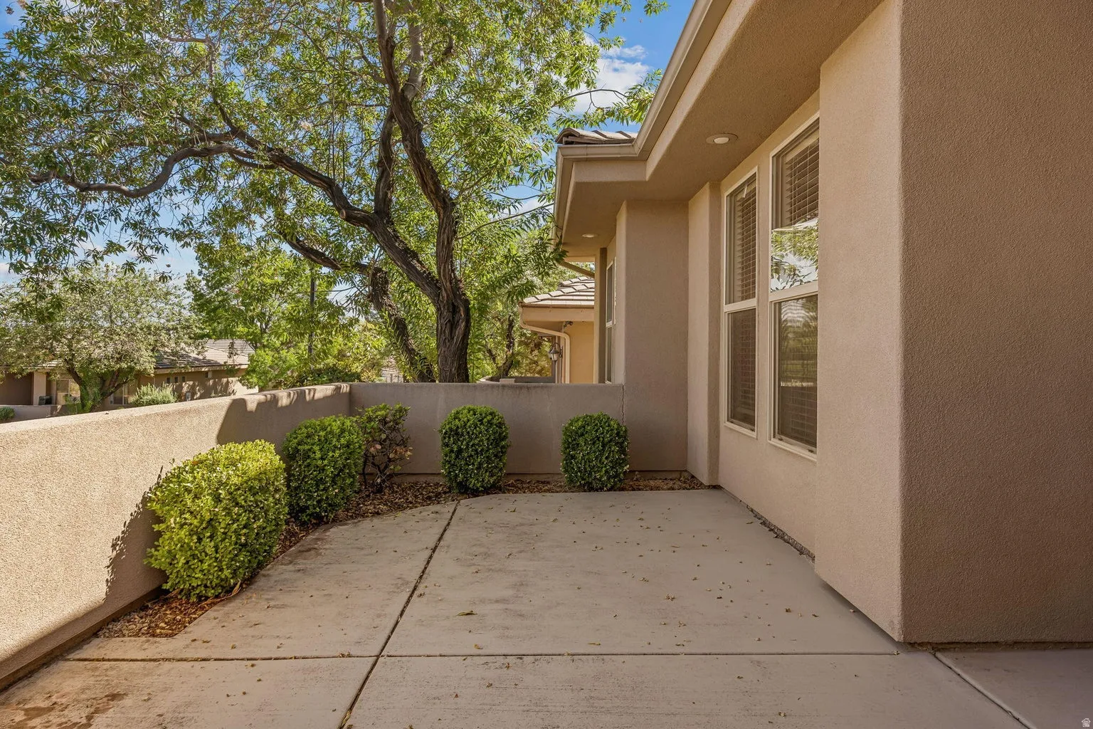 Paved patio area, stucco exterior, multiple windows, recessed lighting, and established shrubbery