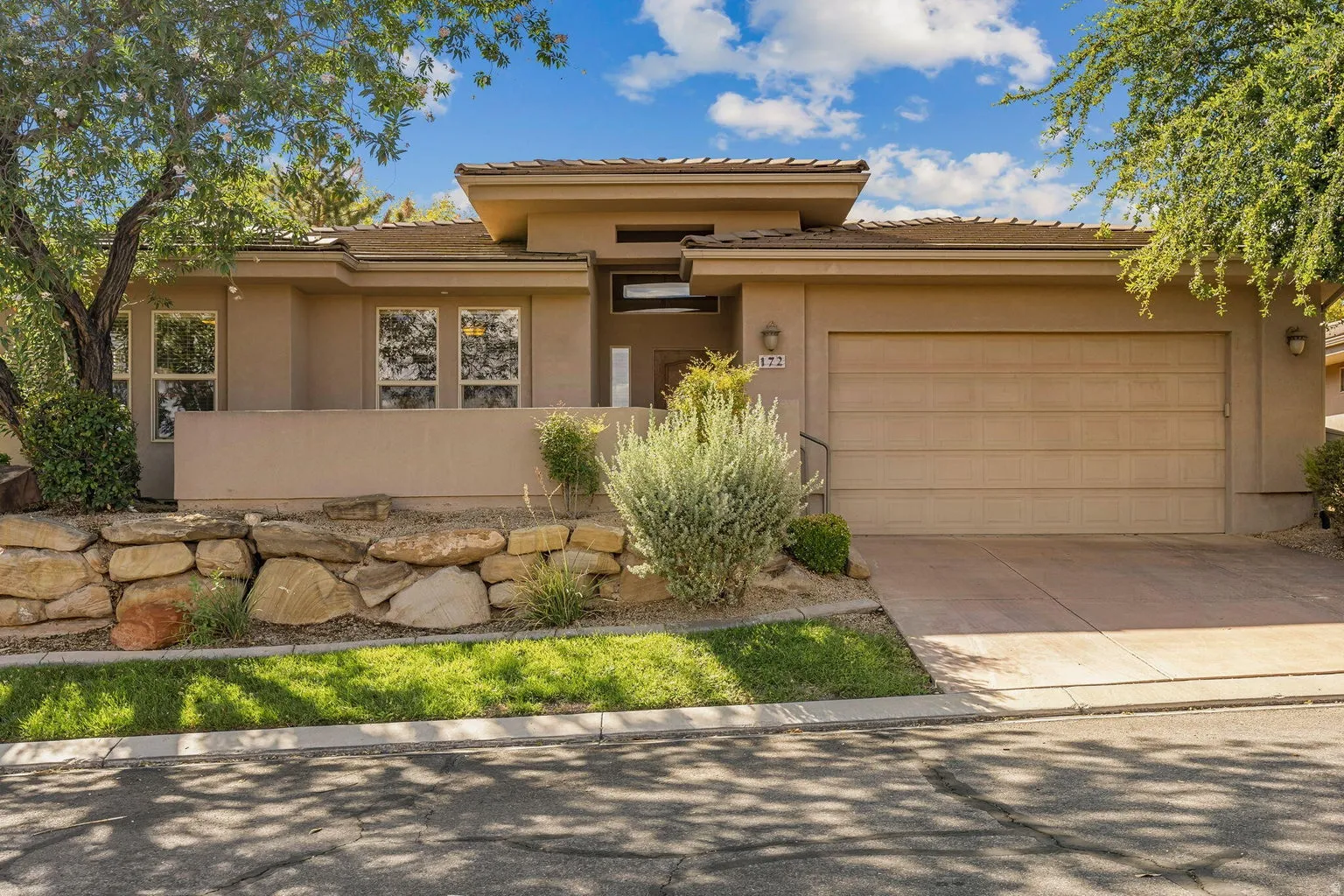 Contemporary stucco exterior with a multi-pane garage door, concrete driveway, and a stone retaining wall