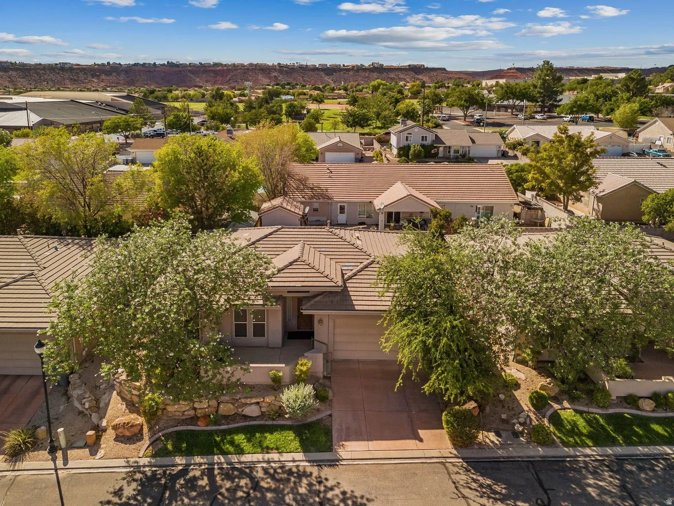 Tile roof, attached garage, paved driveway, mature trees, and landscaping with stone retaining walls