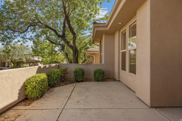 Paved patio area, stucco exterior, multiple windows, recessed lighting, and established shrubbery