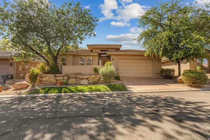 Contemporary stucco exterior with an attached garage, paver driveway, and mature landscaping