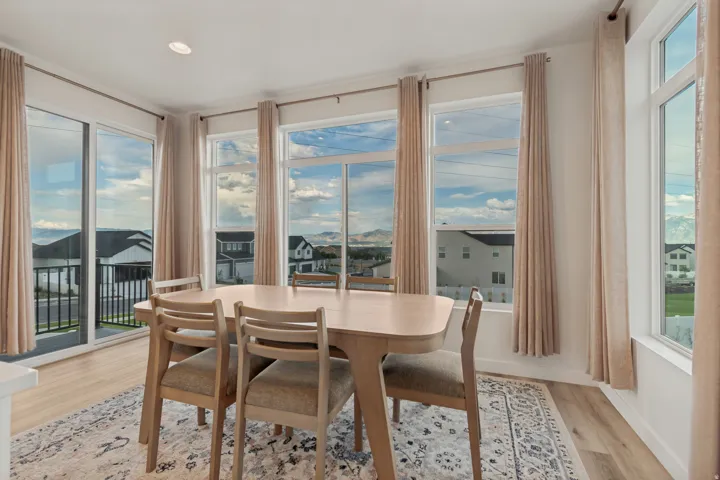 Spacious dining area with light wood-finish flooring, recessed lighting, and multiple large windows