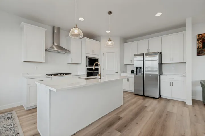 White cabinetry, stainless steel appliances, central island with sink, pendant lighting, and wood-finish flooring