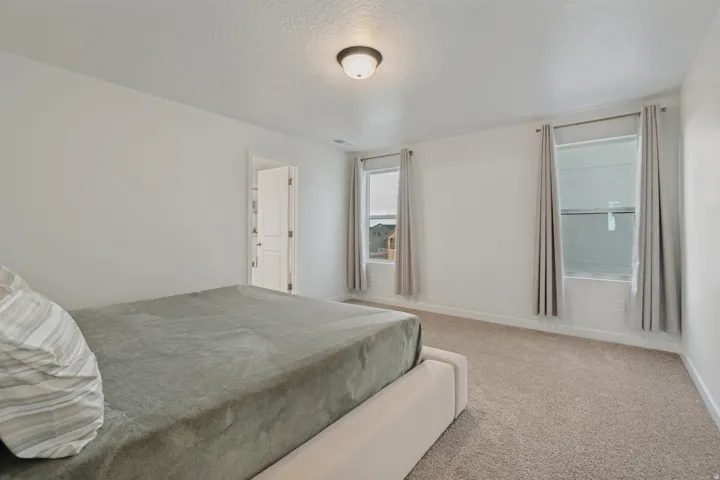 Carpeted flooring, white walls, and two windows with light-colored drapes